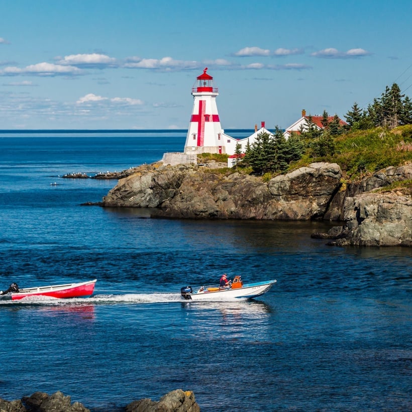Red and white striped lighthouse on rocky coastal cliff with boats in blue water below